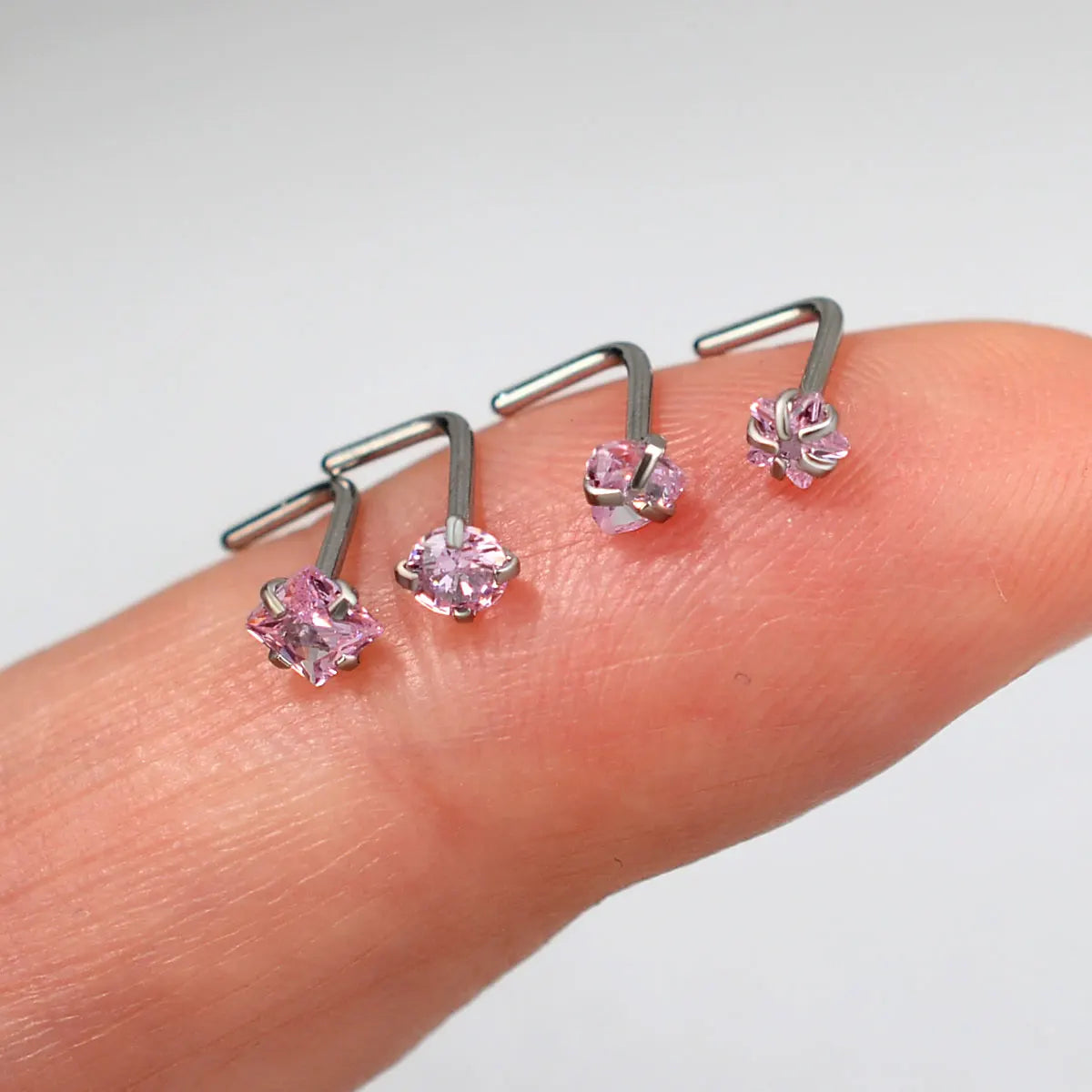 Una mano sostiene un par de pendientes en forma de L de acero inoxidable con detalles de piedra rosa.