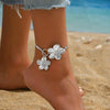 Silver floral pendant necklace and earring set worn on a person's wrist in a beach setting
