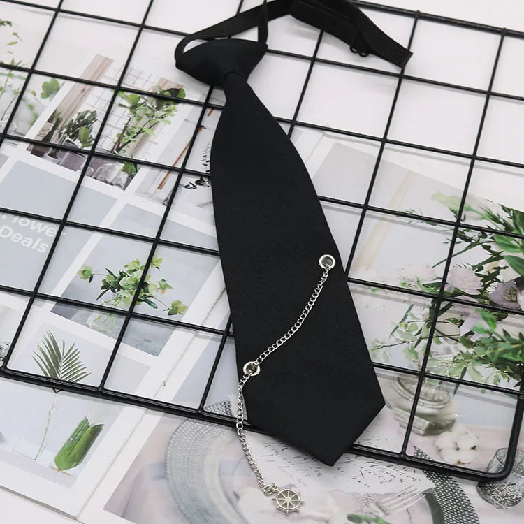 A black pre-tied chain necktie is displayed on a grid background of greenery and paper.