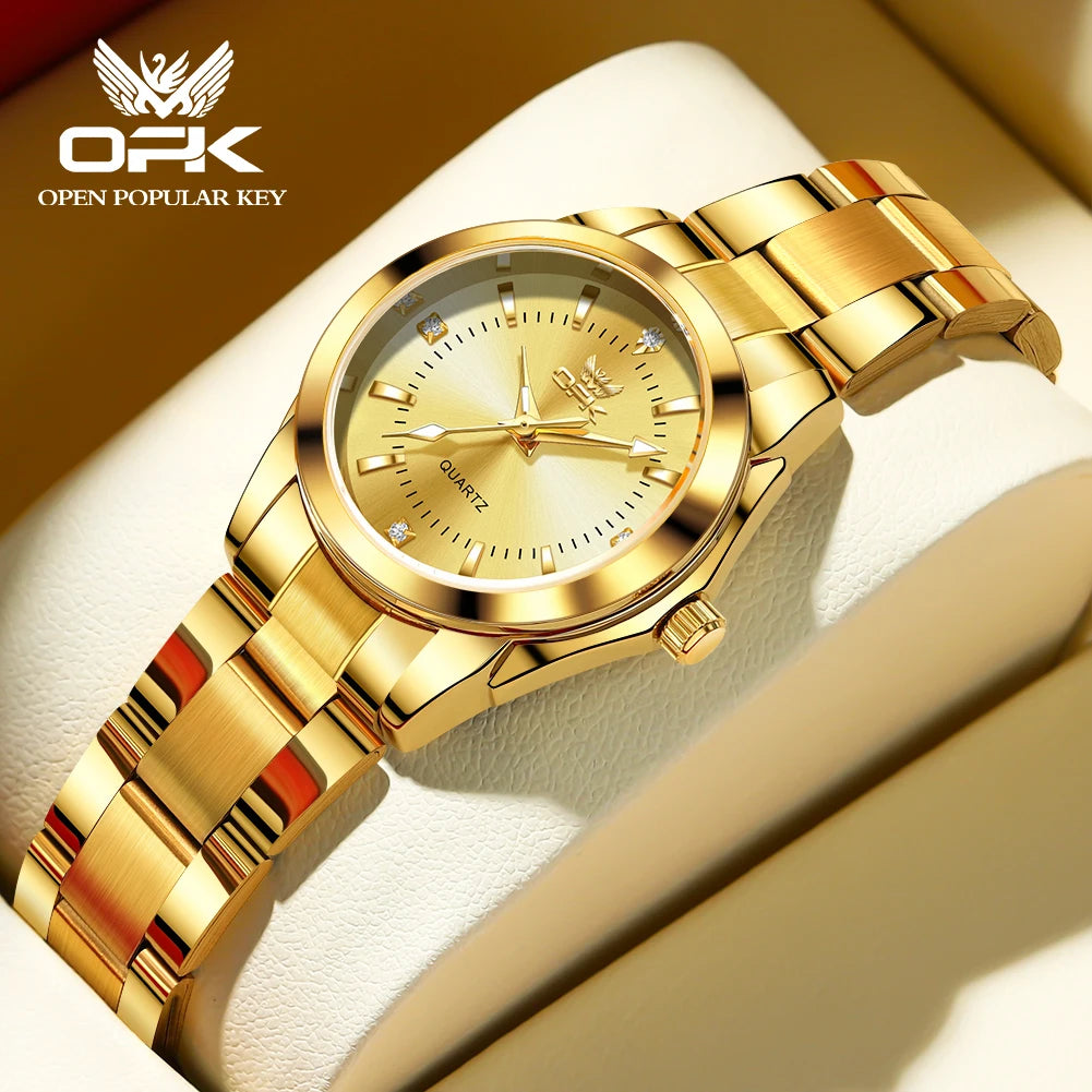 A gold-toned luminous quartz watch with a gold bracelet resting on a light beige surface.