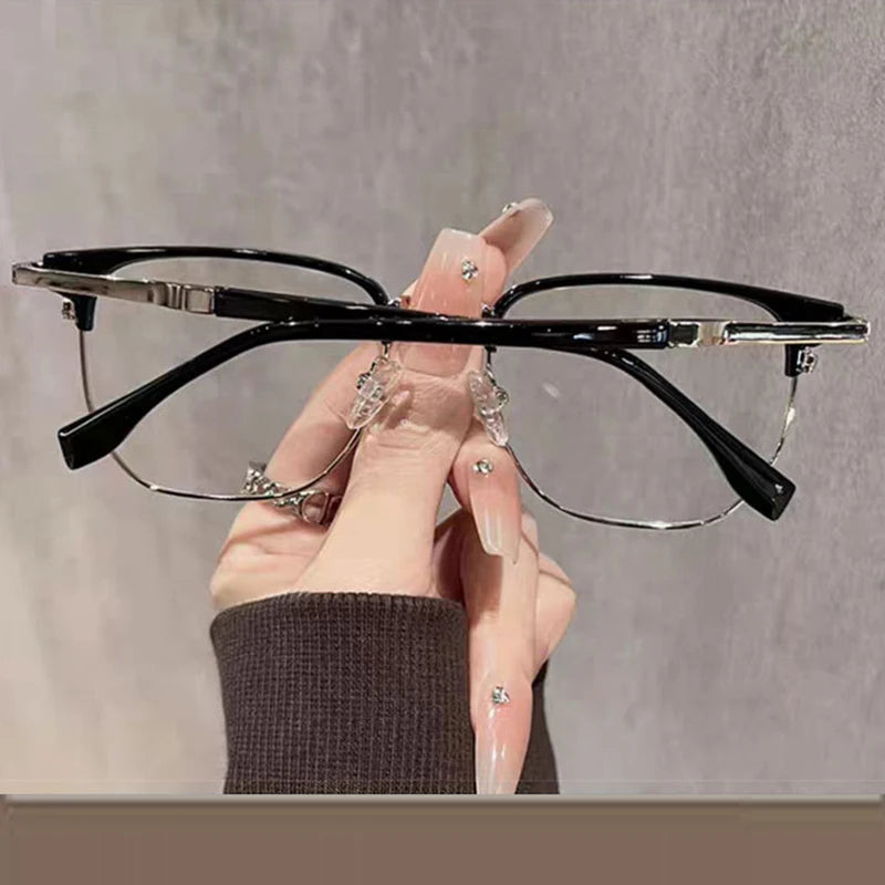 Eine Hand hält eine schwarze Anti-Blaulicht-Lesebrille mit silbernen Akzenten vor einem hellgrauen Hintergrund.