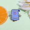 A small enamel pin shaped like a blue cartoon character wearing a blue tunic, placed next to an orange slice and white floral