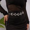 A woman wearing a black dress with a silver heart waist chain body jewelry around her waist.