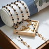 Gold and black crystal bead lanyards and chains displayed next to a rolled white fabric and a wooden frame.