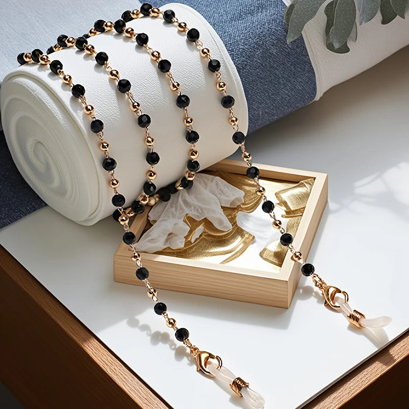 Gold and black crystal bead lanyards and chains displayed next to a rolled white fabric and a wooden frame.