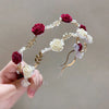 A hand holds an elegant rose vine headband hair accessory featuring deep red and cream fabric roses and delicate gold accents