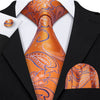 A close-up of an orange and blue patterned silk jacquard tie worn with a black suit jacket and white shirt.