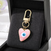 Gold heart keychain featuring a pink and white evil eye design displayed in a black velvet box.