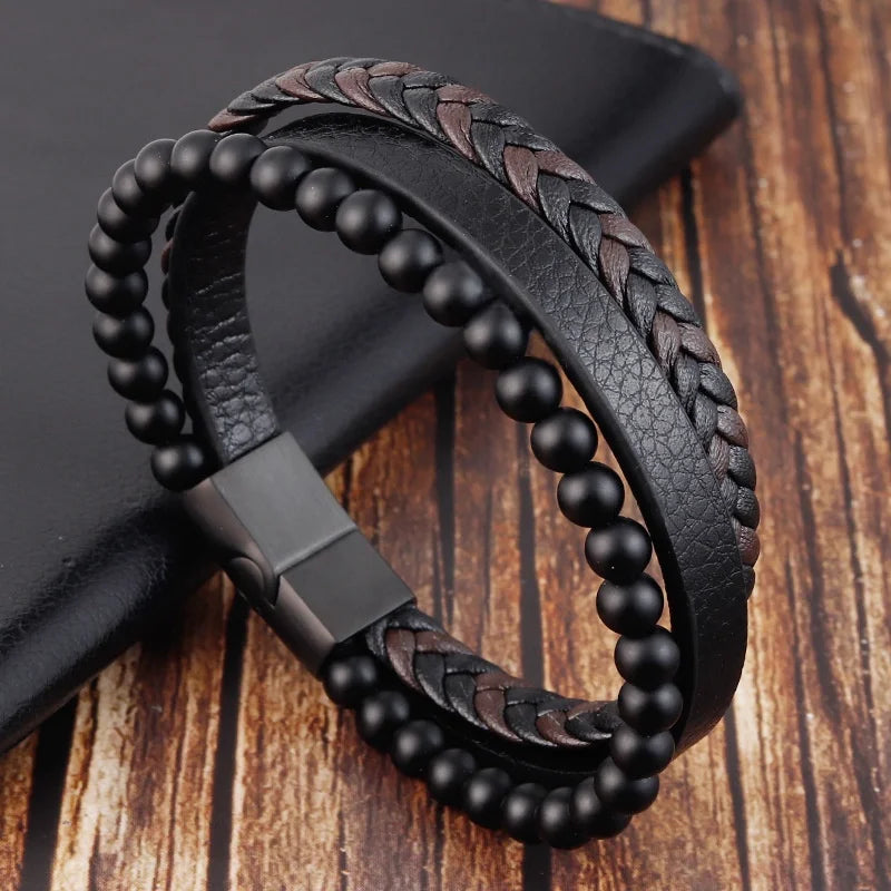 A black leather bracelet featuring a braided design and black beads, resting on a dark surface.