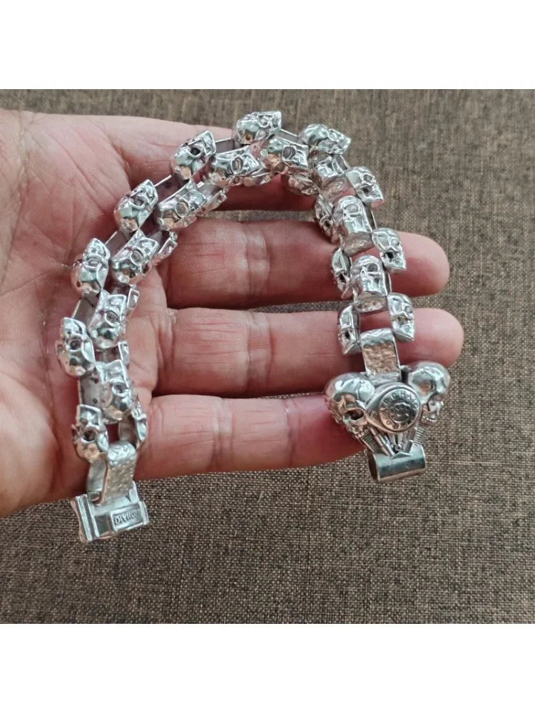 Silberner Schädelarmband für Männer auf der Hand vor braunem Stoffhintergrund.