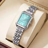 Reloj analógico de cuarzo plateado con esfera azul claro y pulsera de metal, mostrado en una caja de color crema.