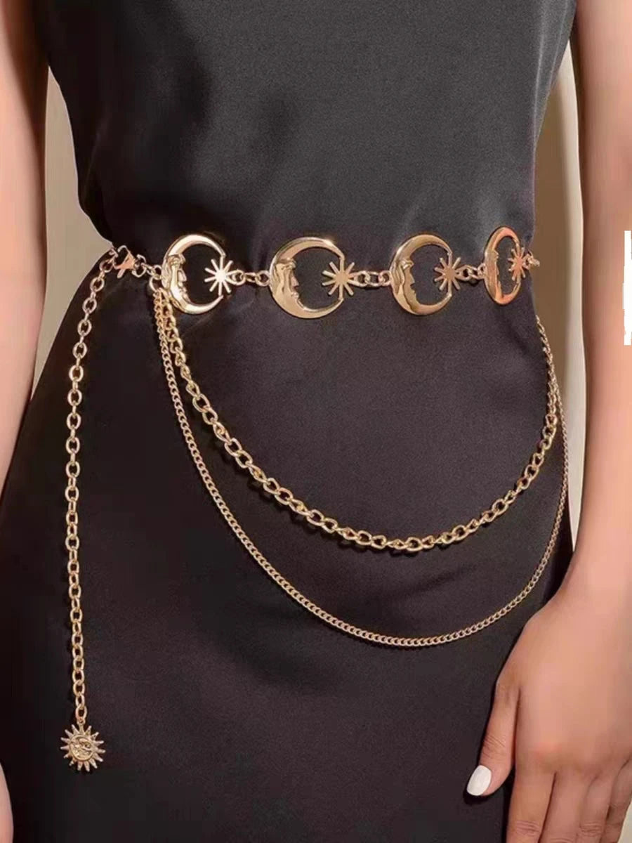 Eine Frau in einem schwarzen Kleid mit goldener Boho-Mond-Fransen-Taillenkette und übereinanderliegenden goldenen Ketten.