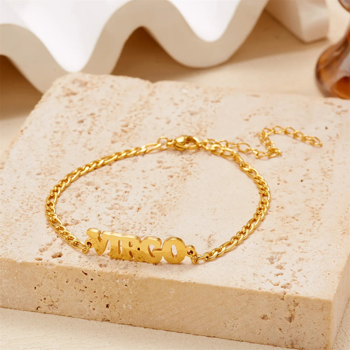 Gold stainless steel Virgo zodiac constellation charm bracelet resting on a light beige surface.