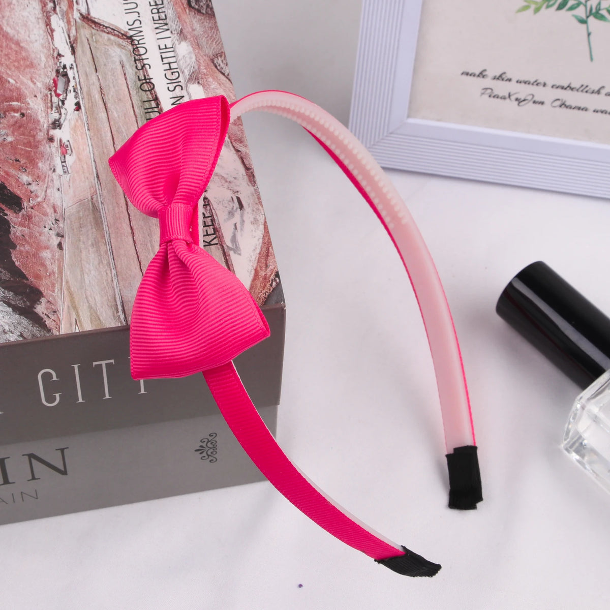A pink grosgrain ribbon hair bow with black accents is displayed next to a box and a framed picture.