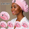 A collection of pink satin hair caps with individual letters printed on them, shown next to a model.