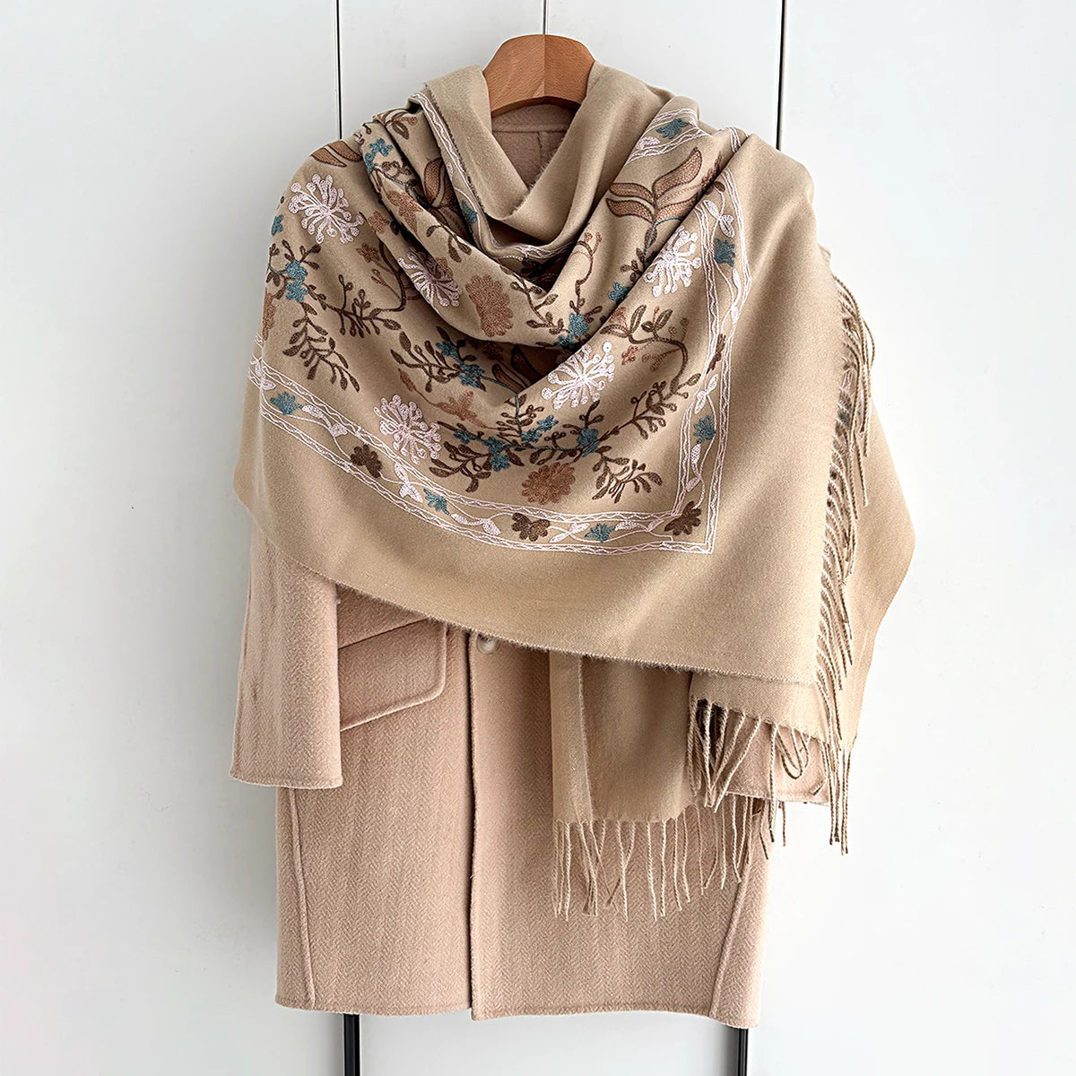 A beige luxury floral scarf draped over a wooden hanger.
