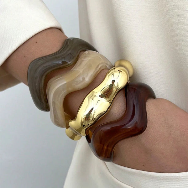 A set of vintage minimalist wavy bangle bracelets in shades of brown, beige, and gold worn on a wrist.