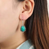 Silver dangle earrings featuring a vibrant turquoise stone set against a dark brown hair background.