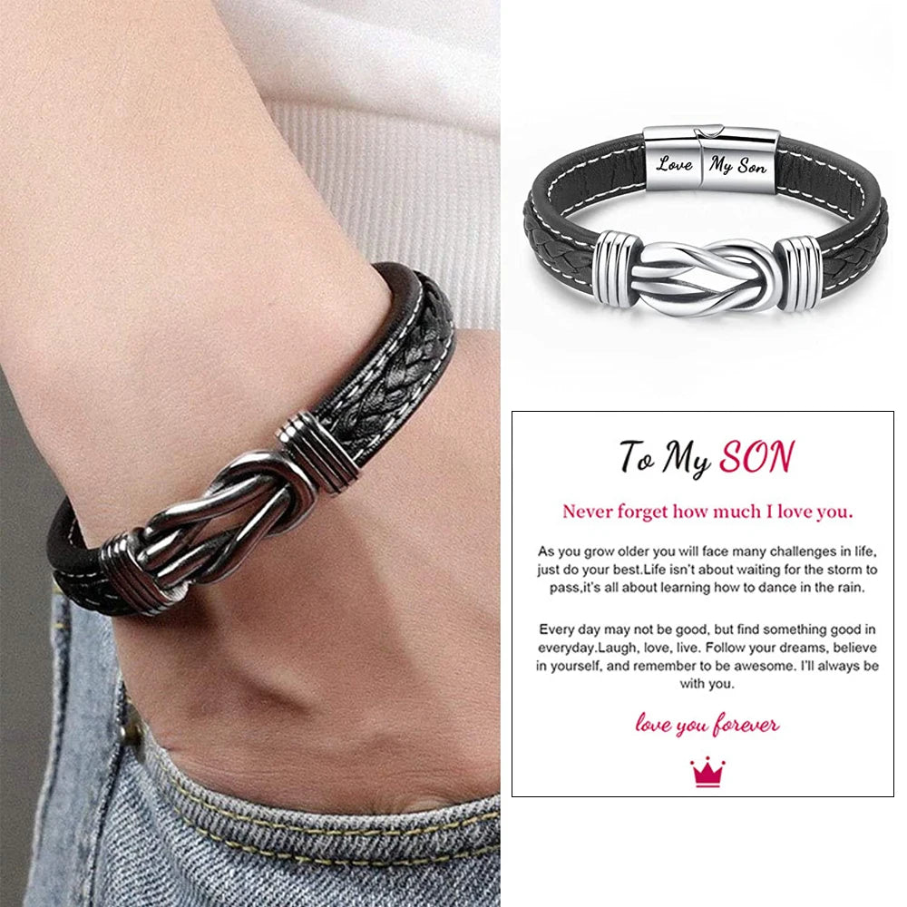 A close-up of a black leather knot bracelet worn on a wrist, with a personalized engraving 'Love My Son' visible.