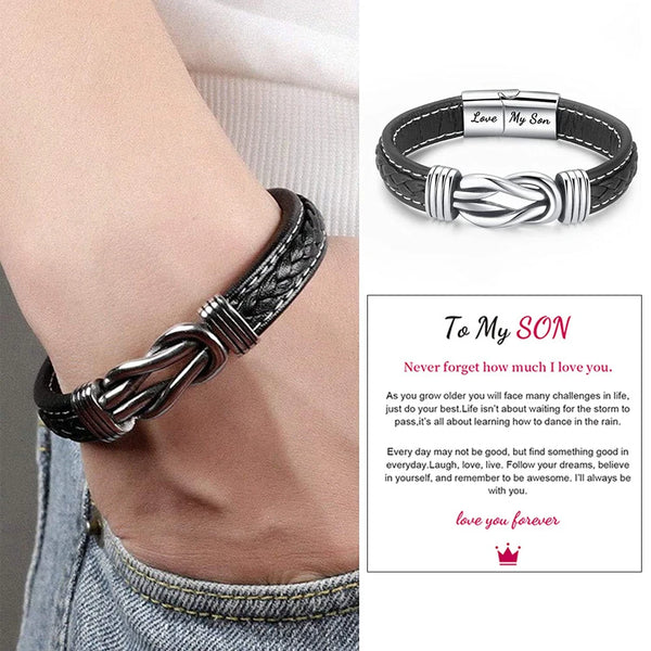 A close-up of a black leather knot bracelet worn on a wrist, with a personalized engraving 'Love My Son' visible.