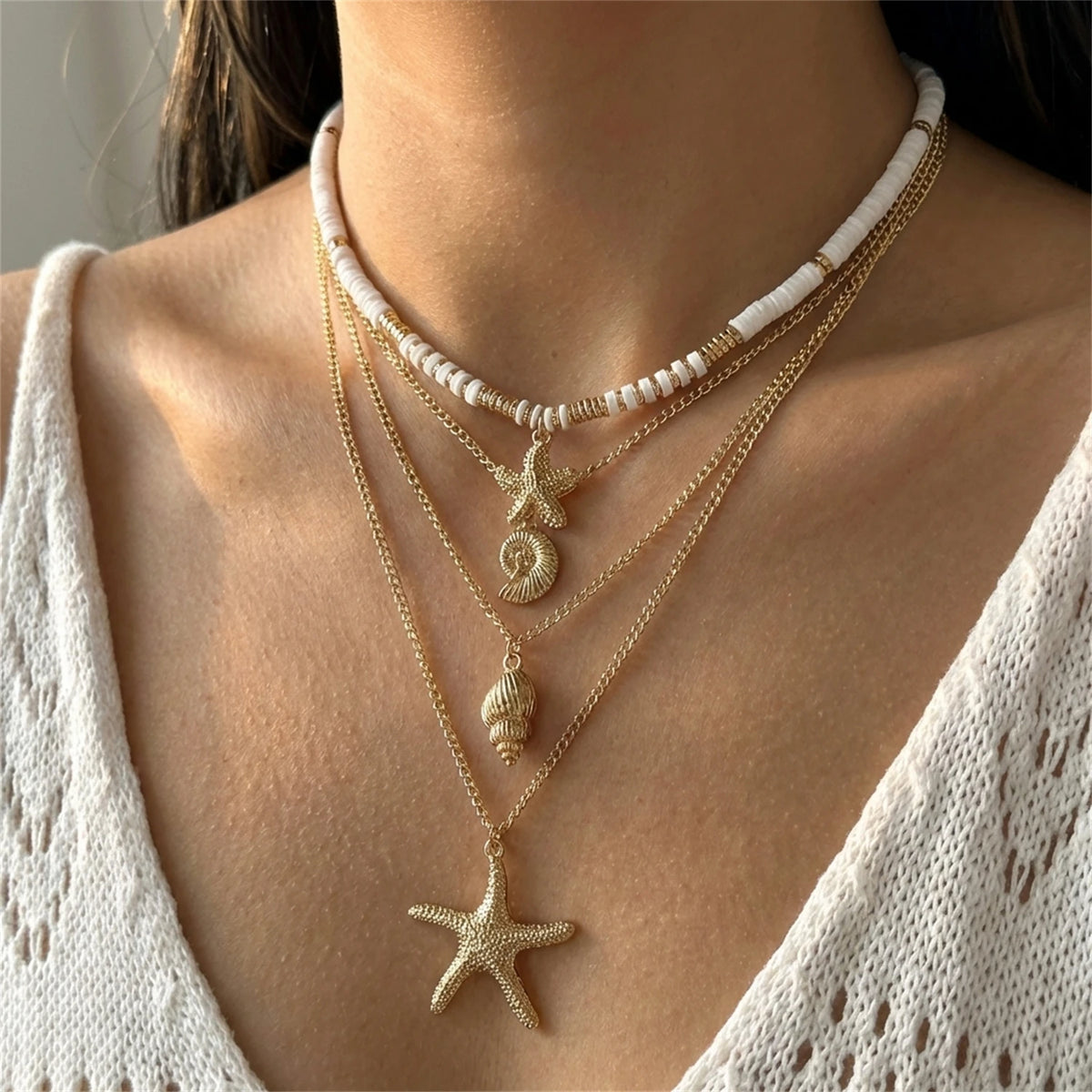 Gold and white beaded necklace featuring a starfish pendant worn against a white knit top.