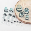 A collection of glass ear stretching plugs and tunnels arranged on a wooden slice.