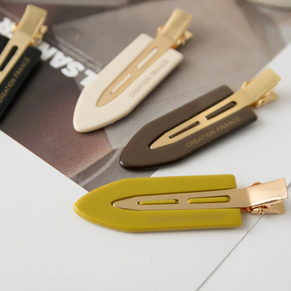 Three seamless hair clips in gold, beige, and olive green are displayed on a dark background.
