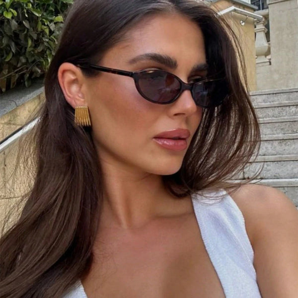 امرأة بشعر داكن طويل ترتدي نظارات شمسية بإطار بيضاوي قديم في الخارج.