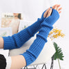 A pair of blue knitted fingerless gloves being held up against a white background.