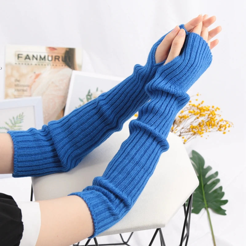 A pair of blue knitted fingerless gloves being held up against a white background.