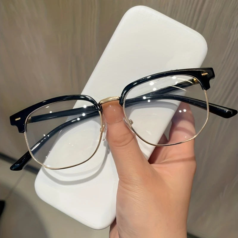 A hand holds a pair of black eyeglasses with gold accents against a white background.