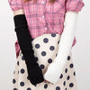 A person wearing a pink plaid shirt and beige polka dot skirt, with black knitted fingerless gloves and white knitted arm war