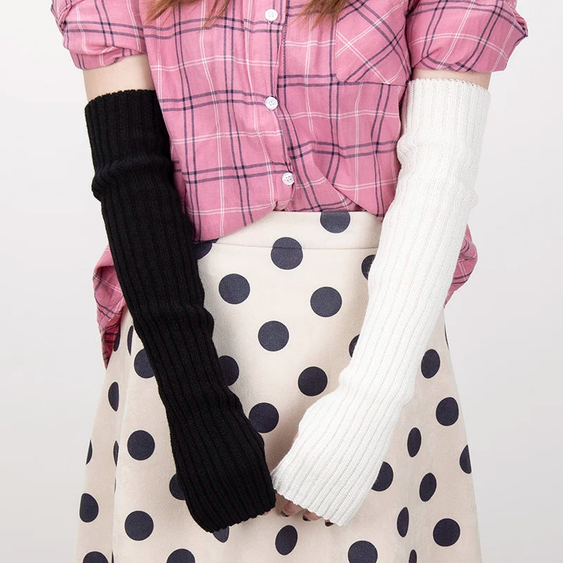 A person wearing a pink plaid shirt and beige polka dot skirt, with black knitted fingerless gloves and white knitted arm war