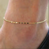 A delicate gold geometric anklet bracelet worn around the ankle of a person.