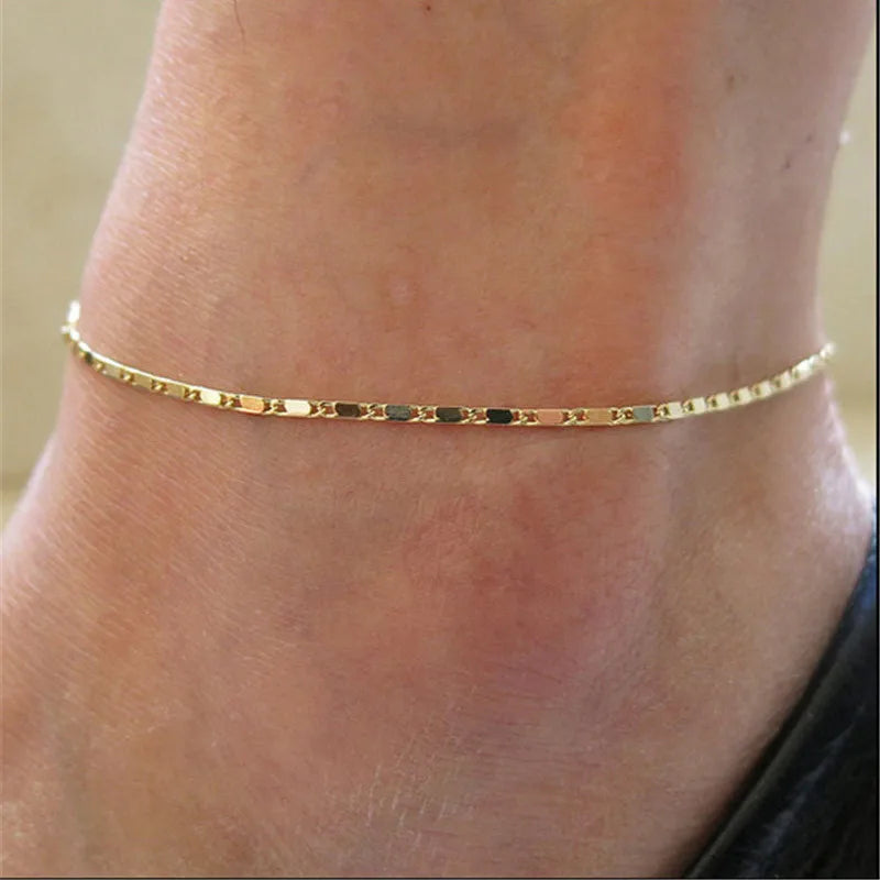 A delicate gold geometric anklet bracelet worn around the ankle of a person.