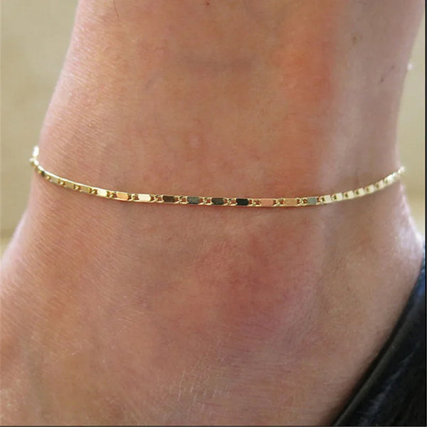 Zartes goldenes geometrisches Fußkettchenarmband, getragen am Knöchel.