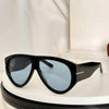 Black oversized pilot sunglasses with dark blue lenses resting on a white surface.