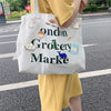 A white tote bag featuring green text that reads Ondon Grocery Marke with various cute animal and rainbow pins.