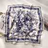 A white silk scarf featuring a detailed purple floral and botanical print.