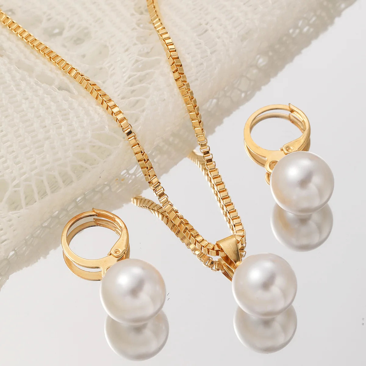 A gold-toned dainty pearl jewelry set featuring a necklace and matching pearl earrings displayed on a sheer fabric.