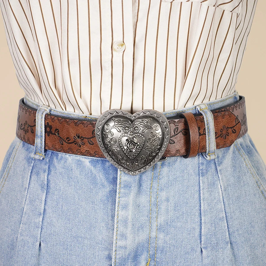A close-up of a woman's torso showing a striped shirt, denim pants, and a heart-shaped retro embossed leather belt.
