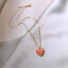 A delicate gold chain necklace featuring a pink crystal heart pendant on a light gray fabric.