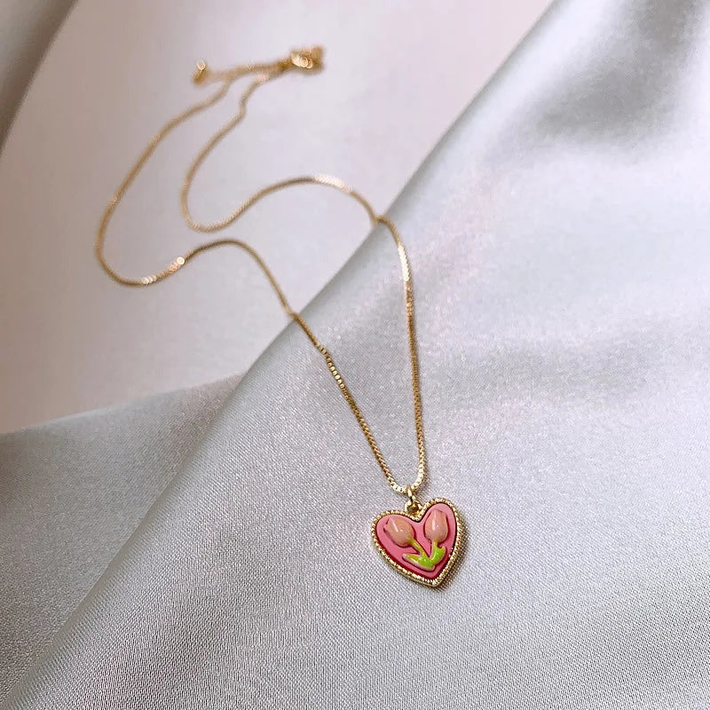 A delicate gold chain necklace featuring a pink crystal heart pendant on a light gray fabric.