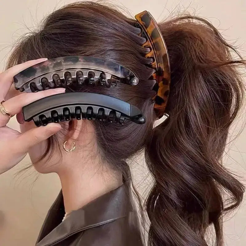 Eine Hand benutzt eine Schmetterlings-Bananenhaarklemme und eine Haarnadel auf dunkelbraunes Haar.