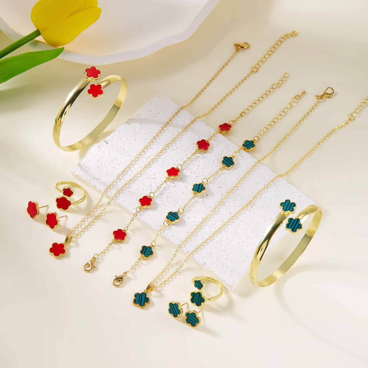 A set of five gold-colored bracelets and rings featuring red and blue enamel plum blossom designs displayed on a white surfac