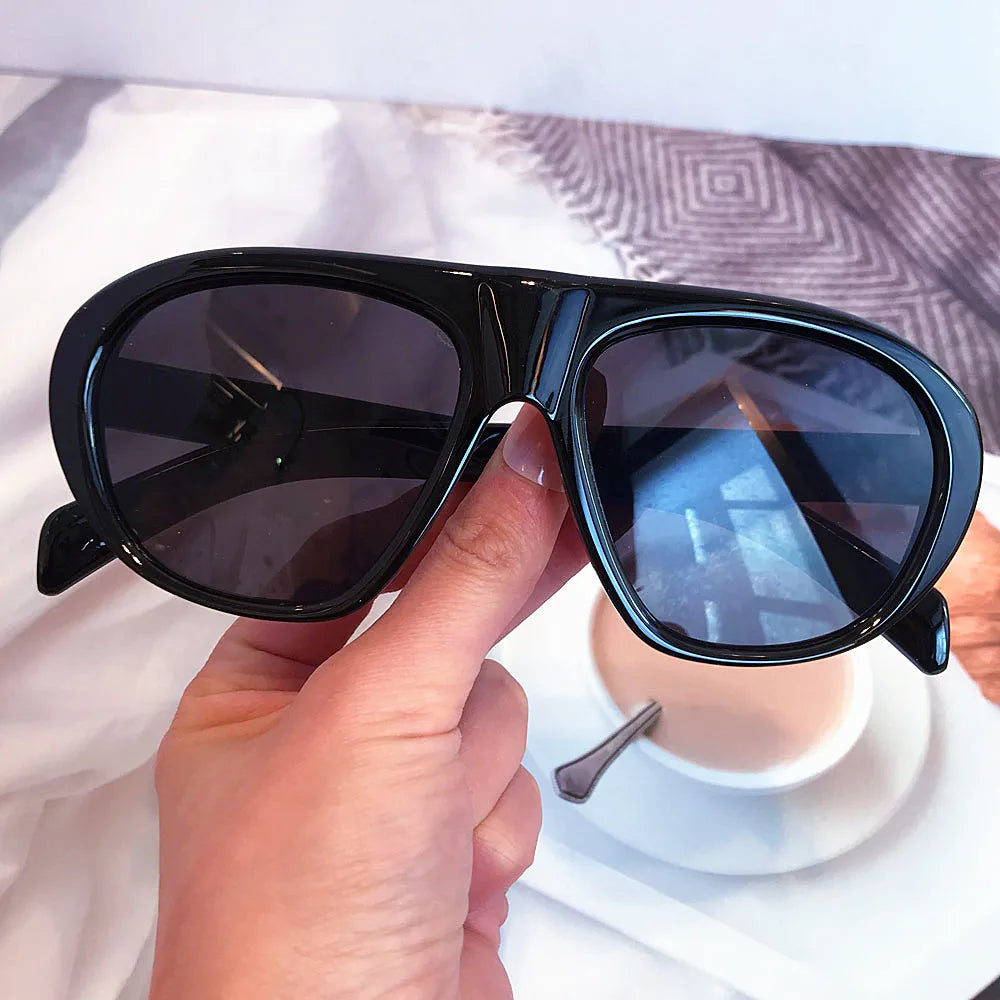 A hand holds a pair of black vintage gradient leopard sunglasses against a white background.