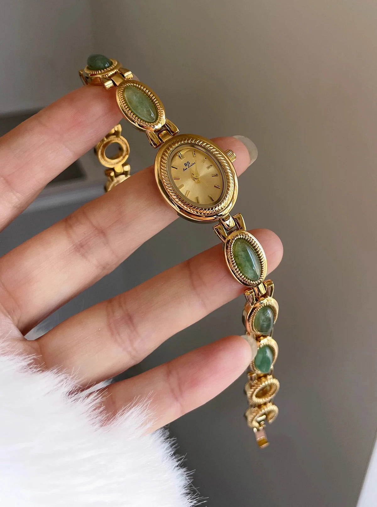 Une main tient une élégante montre-bracelet en or avec des pierres de quartz jade vert sur un bracelet en or.