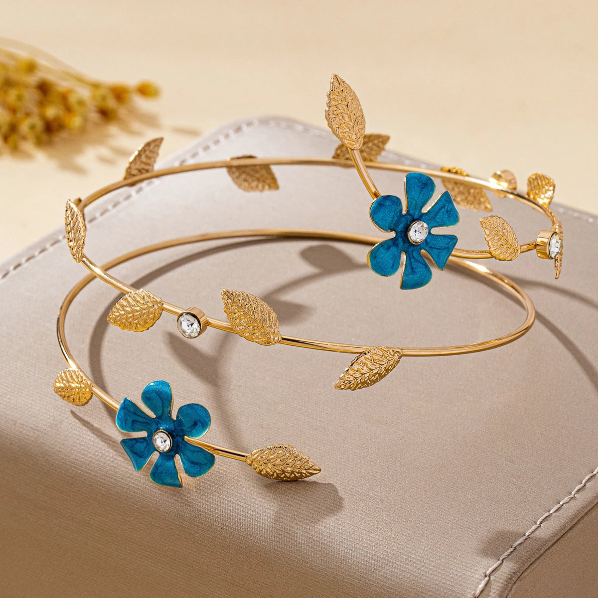Gold floral vine arm bracelet with blue enamel flowers and silver accents displayed on a beige surface.