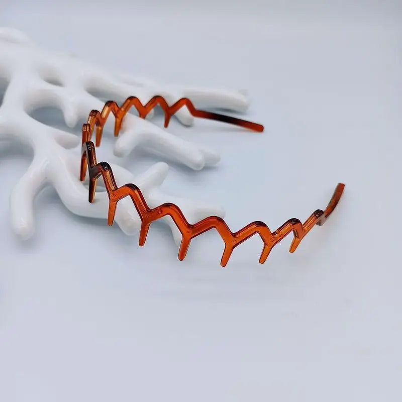 A close-up of anti-slip toothed hair accessories in a coppery orange color resting on a white surface.