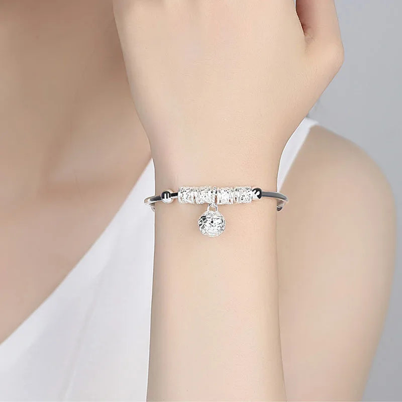 A close-up of a stack of clear diamond and silver bell bangles worn on a wrist.